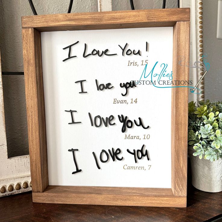 a wooden frame with writing on it sitting next to a potted plant and vase