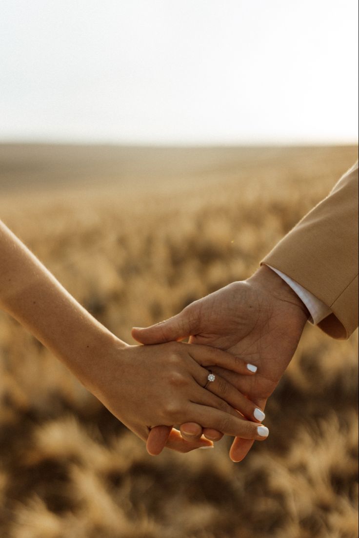 two people holding hands in the middle of a field