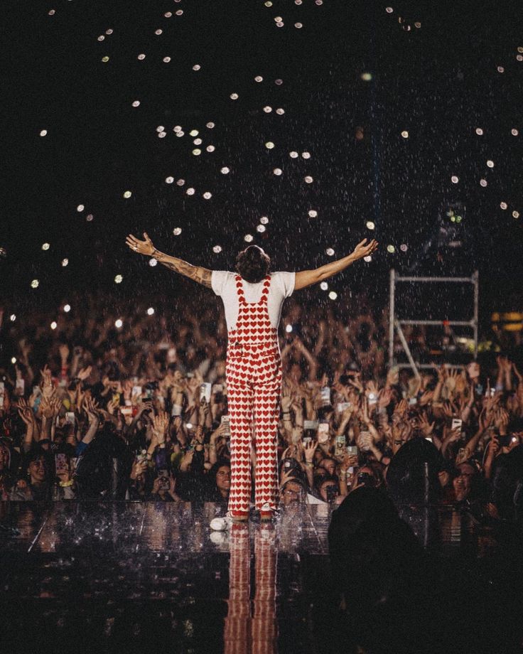 a man in red and white jumpsuit standing on stage with arms spread wide open