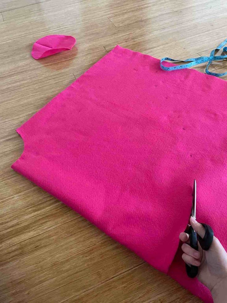 someone is cutting fabric with scissors on the floor next to pink material that has been cut into smaller pieces