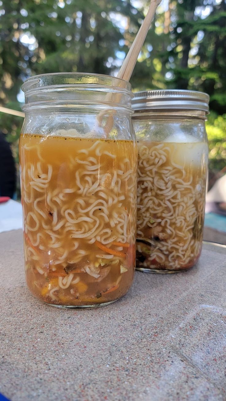 two mason jars filled with food sitting on top of a stone table next to trees