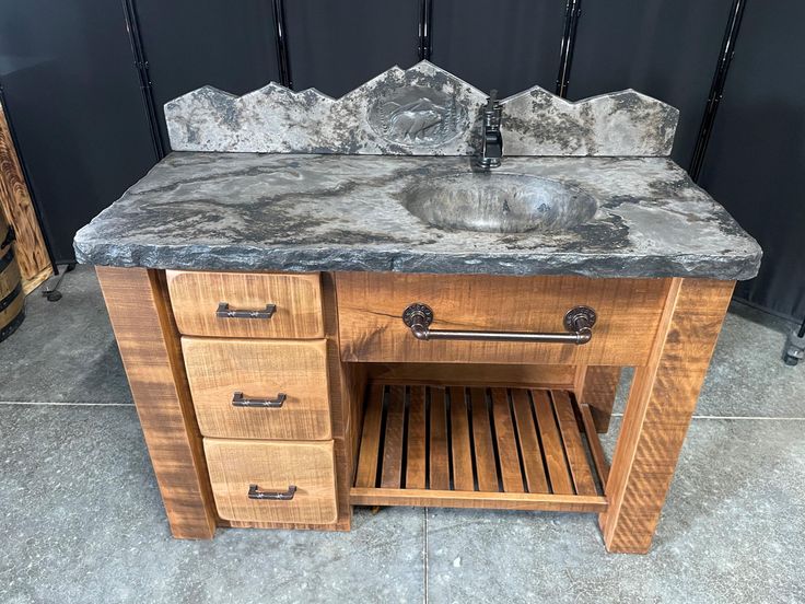 a bathroom vanity with marble top and wooden cabinet drawers in front of a black wall