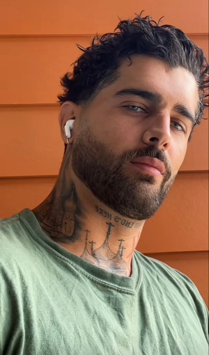 a man with tattoos and piercings on his neck looking off to the side in front of an orange wall