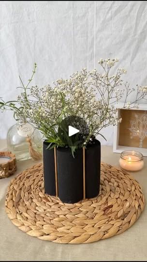 a table topped with two black vases filled with flowers and greenery on top of a woven place mat