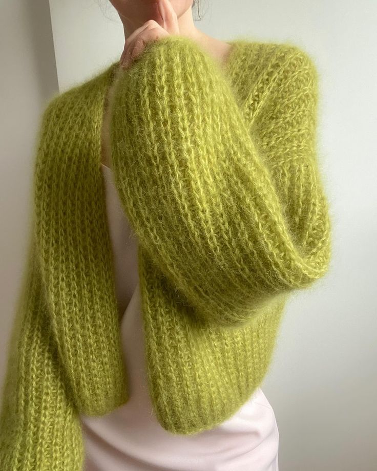 a woman wearing a green knitted cardigan with her hands on her chin and looking at the camera