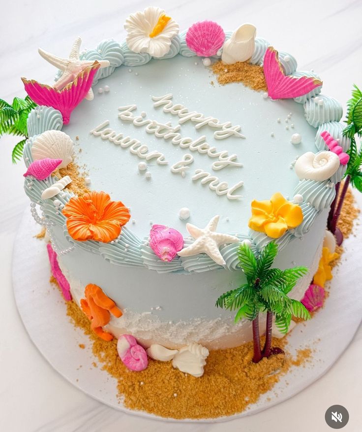 a birthday cake decorated with seashells and flowers on a white tableclothed surface