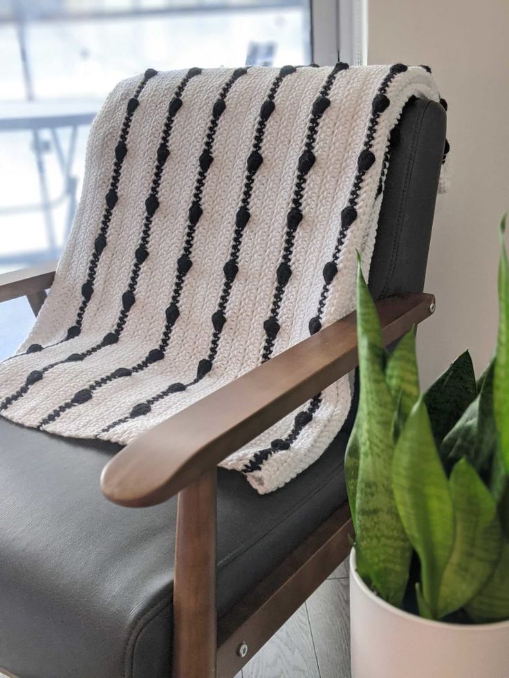 a black and white blanket sitting on top of a chair next to a potted plant