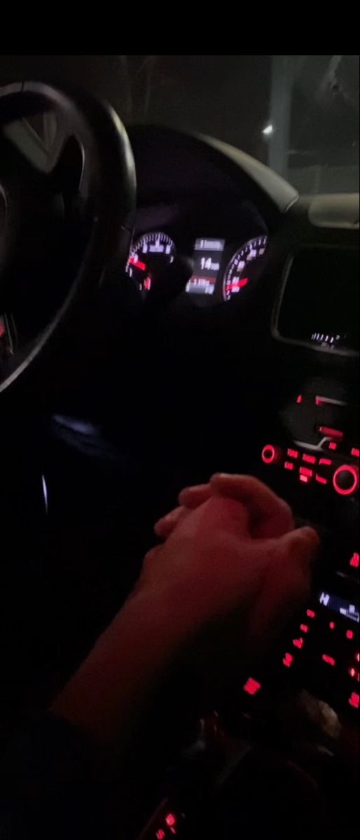 a person driving a car at night with red lights on the dashboard and steering wheel