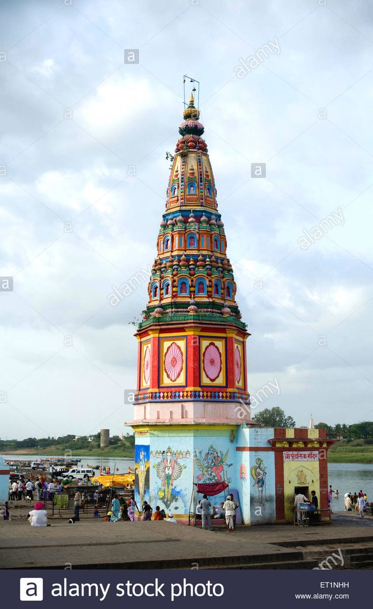 the colorful tower is on display in front of some water and people walking around it