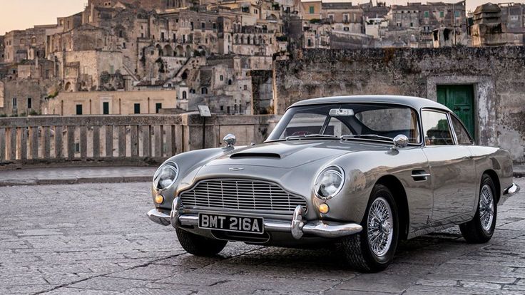 an old silver car parked in front of a building with lots of buildings behind it