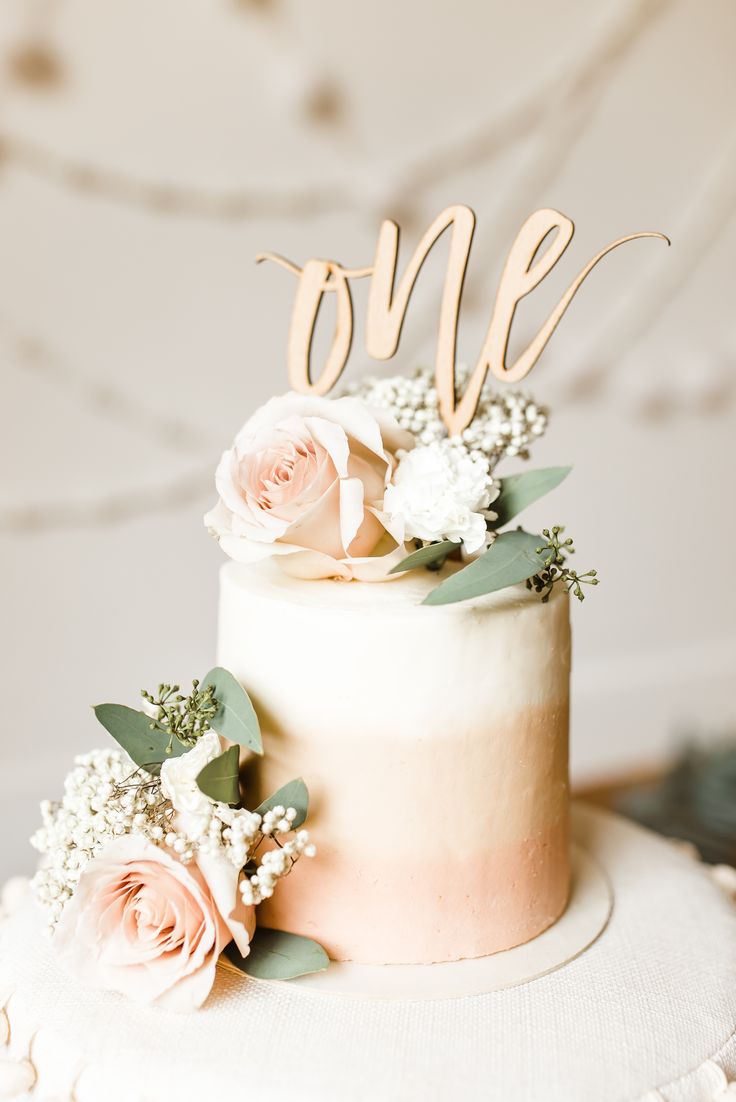 a wedding cake with flowers on top and the word one spelled out in cursive letters