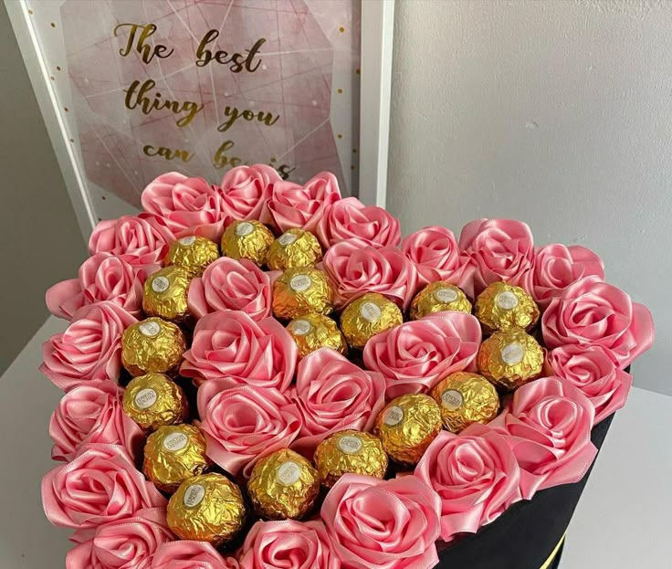 a heart shaped box filled with pink roses and gold foiled chocolates next to a card