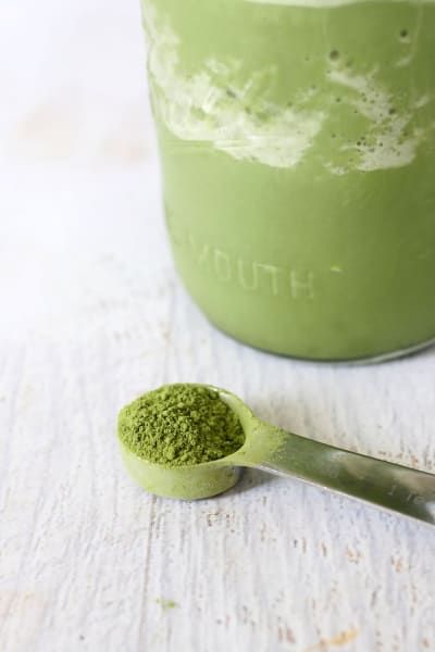 a green powder in a jar with a spoon next to it on a white surface