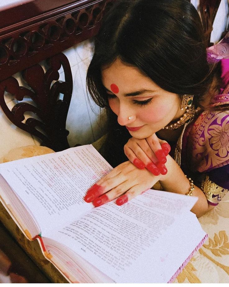 a woman laying down reading a book with her hands on her chin and looking at the pages