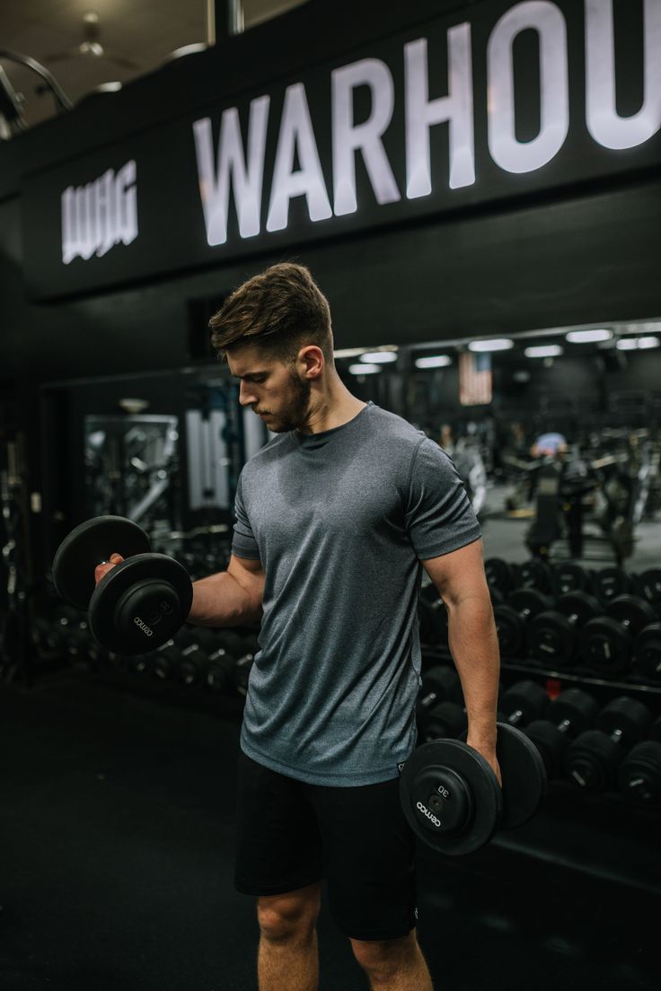 a man holding two dumbs in front of a gym