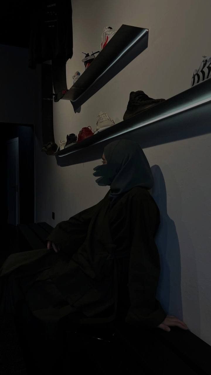 a person in a dark room with shoes hanging on the wall and shelves above them