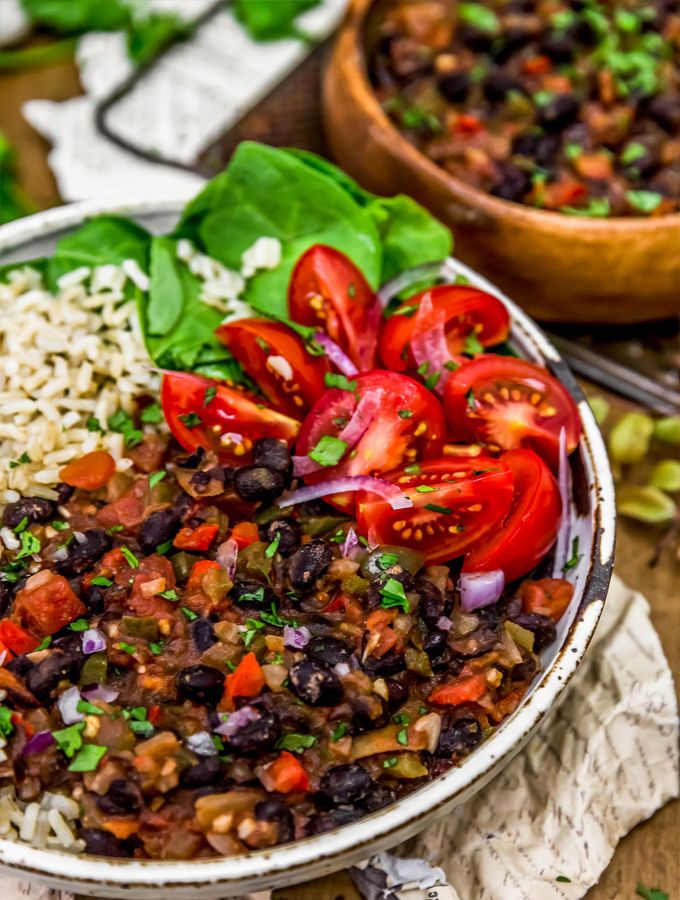 a bowl filled with rice, black beans and tomatoes on top of a wooden table