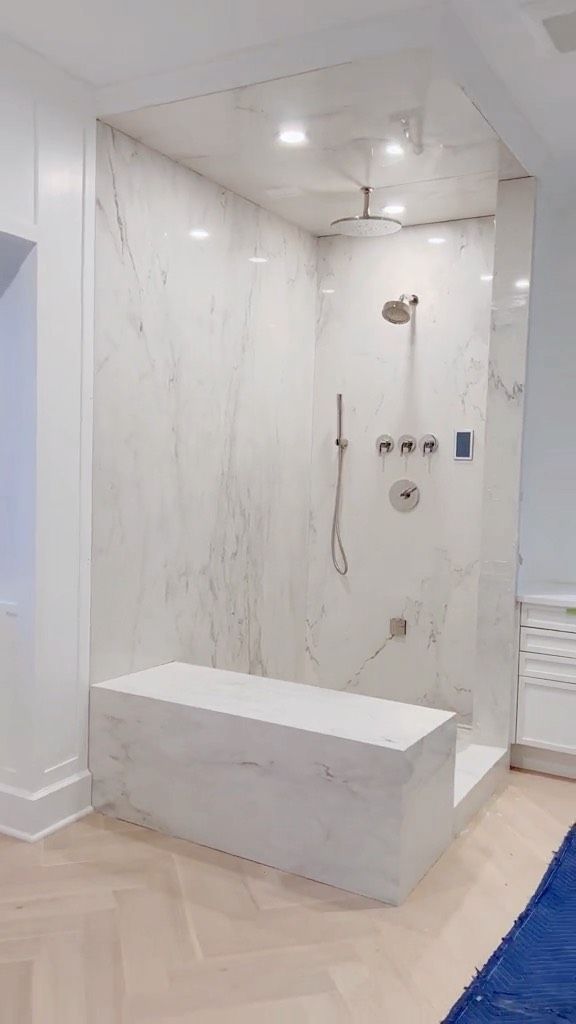 a white bathroom with a walk in shower next to a blue rug and wooden floor