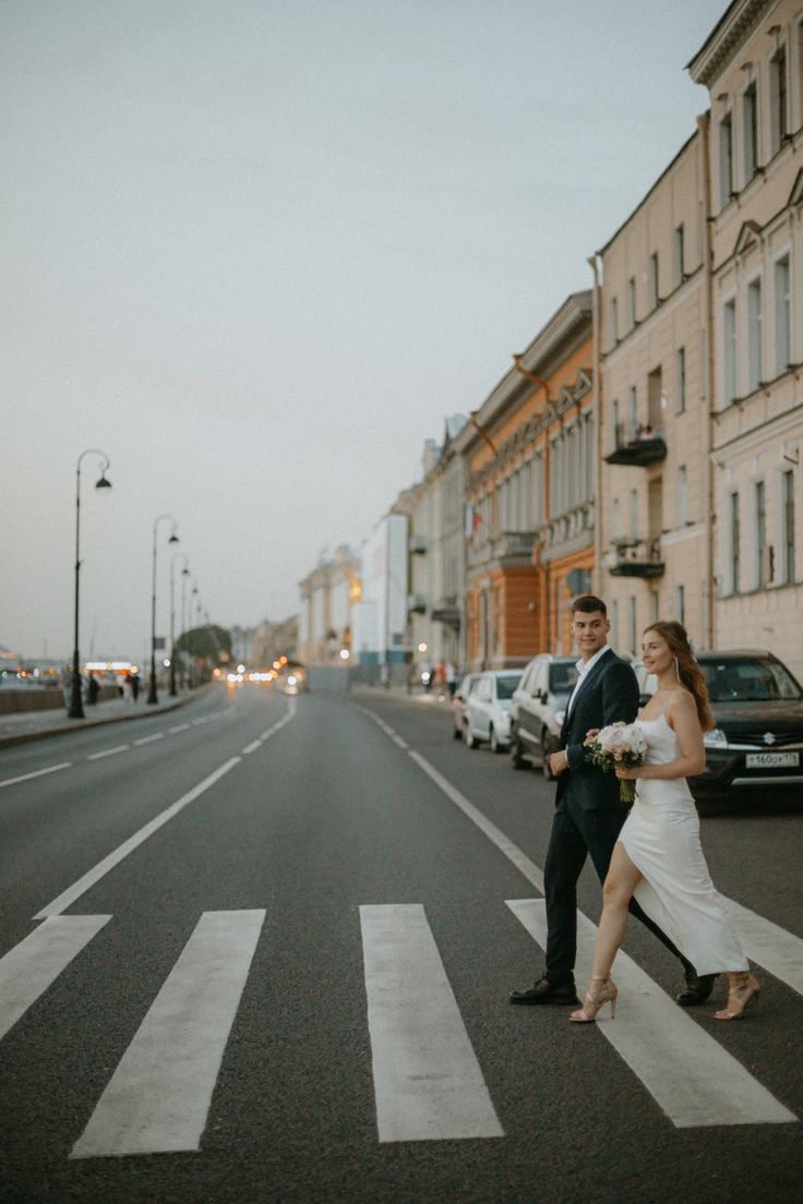 a bride and groom crossing the street in front of an old building on a city street