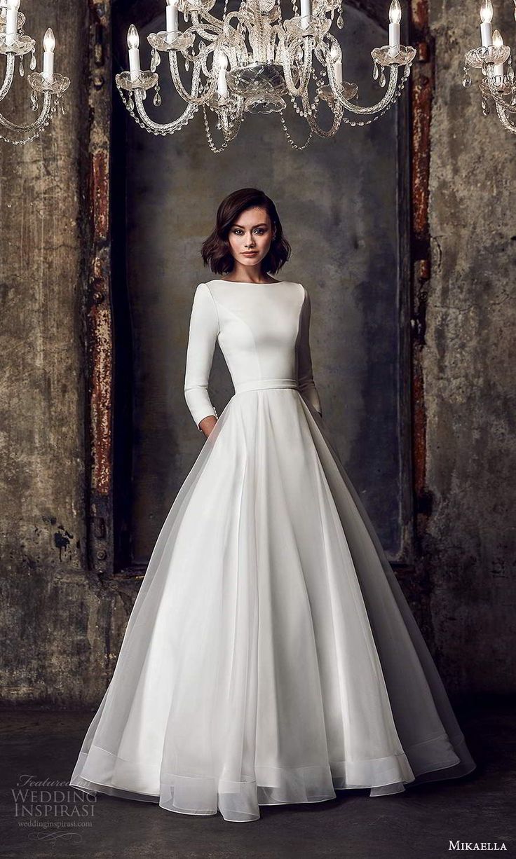 a woman standing in front of a chandelier wearing a white dress with long sleeves