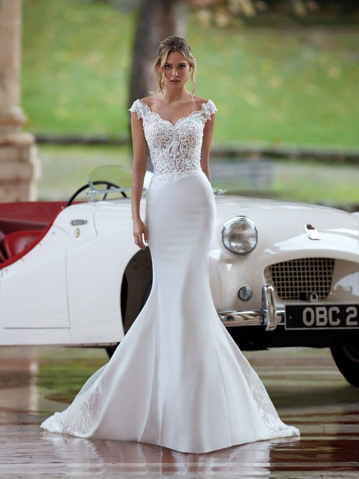 a woman in a wedding dress standing next to an old car