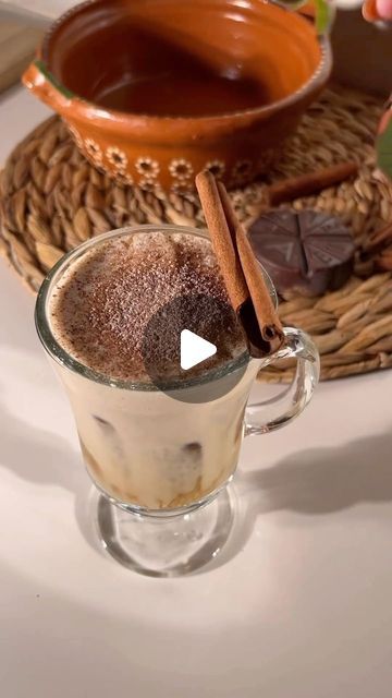 a glass cup filled with hot chocolate and cinnamon sticks on top of a white table