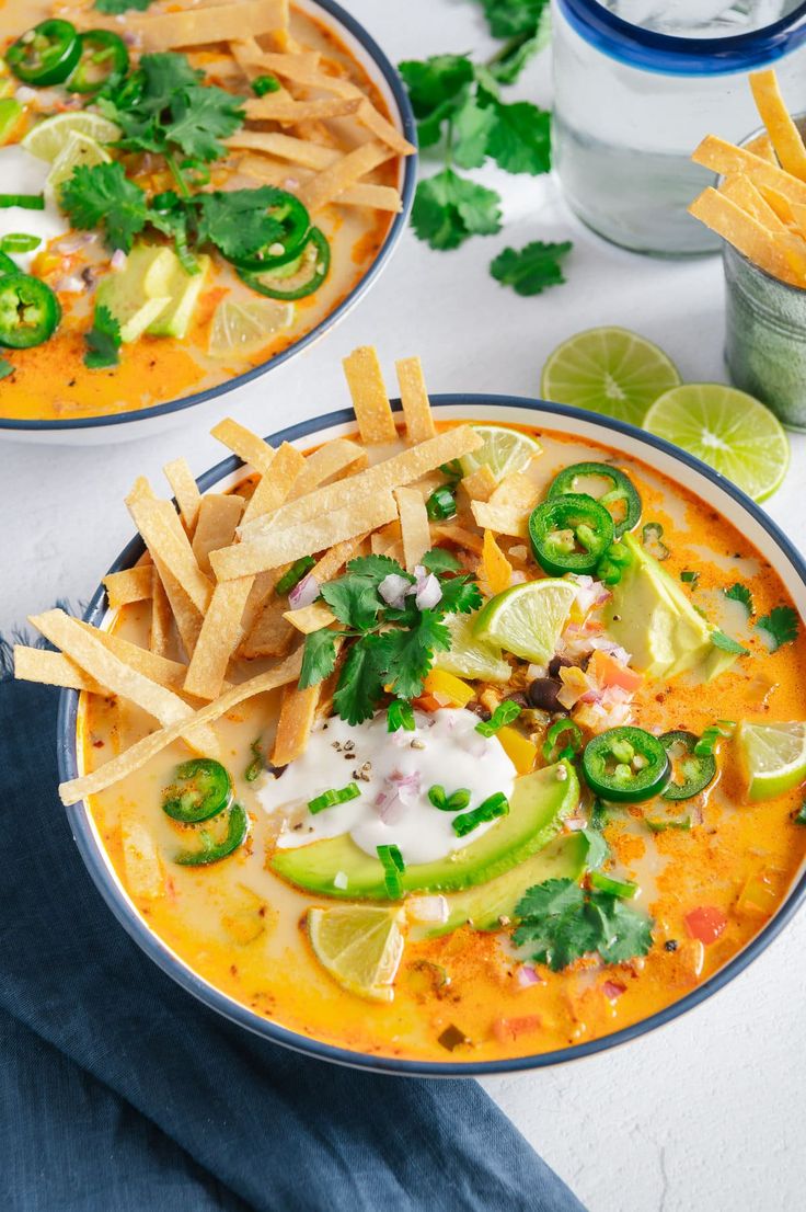 two bowls of mexican soup with tortilla chips and limes on the side