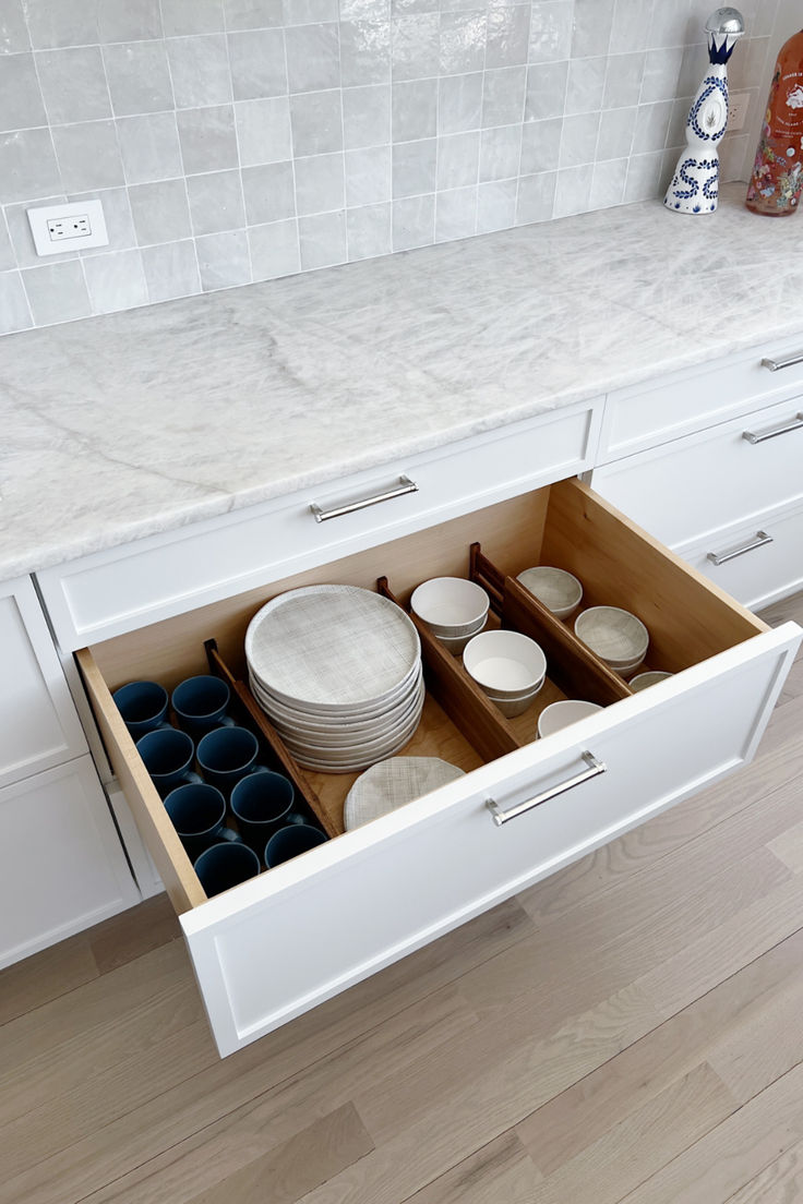 an open drawer in a kitchen filled with plates and bowls on top of a counter