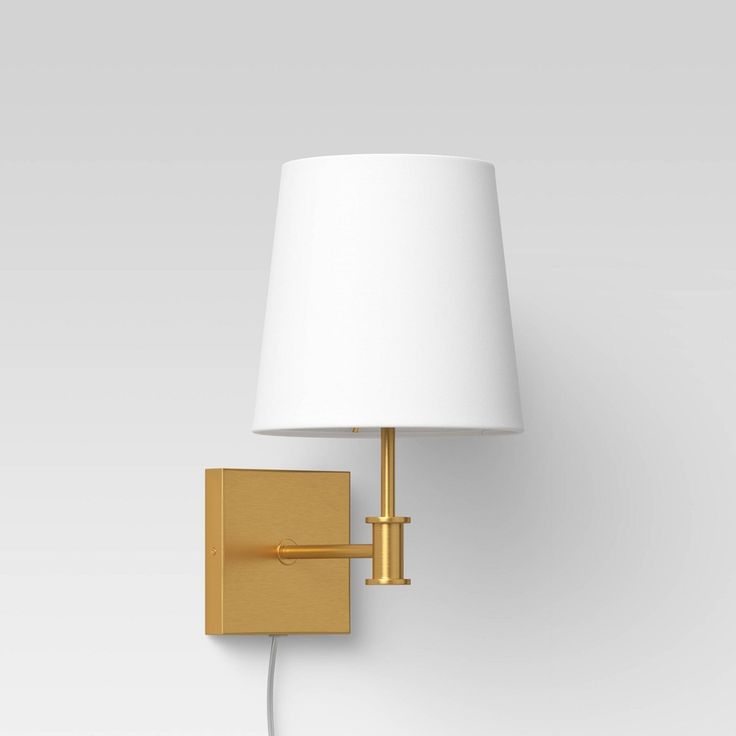 a wall light with a white shade on the side and a gold metal frame around it