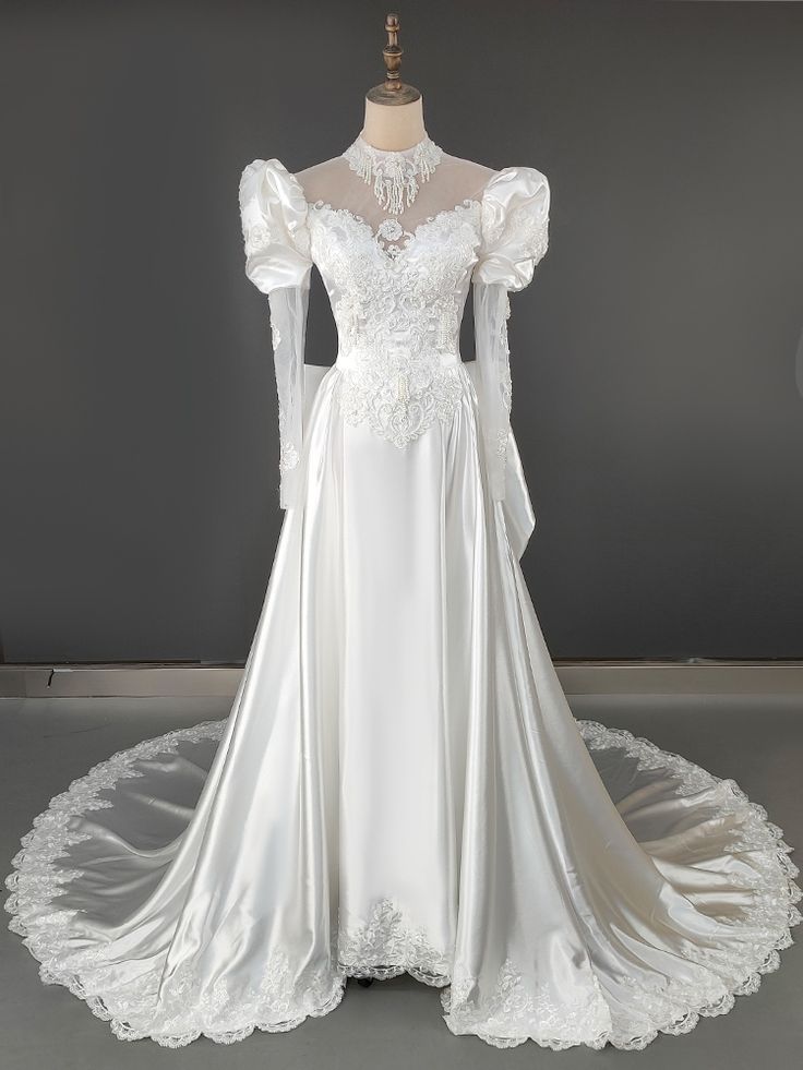 a white wedding dress with long sleeves on display in front of a gray wall and floor