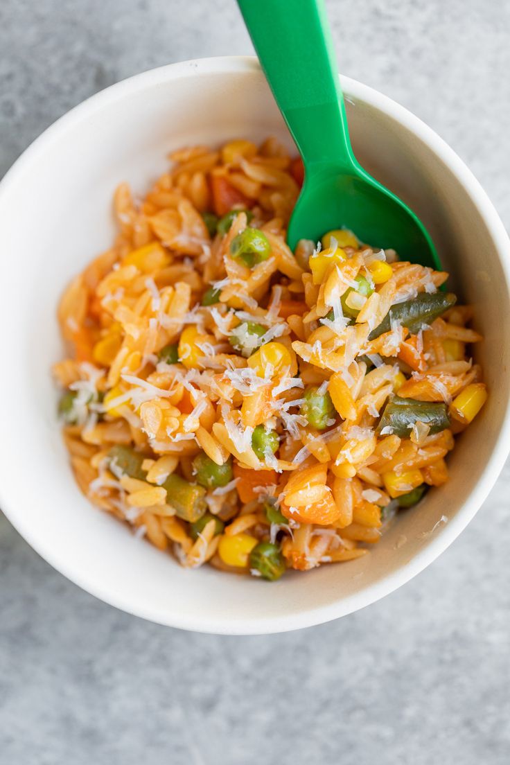 a white bowl filled with rice and veggies next to a green plastic spoon