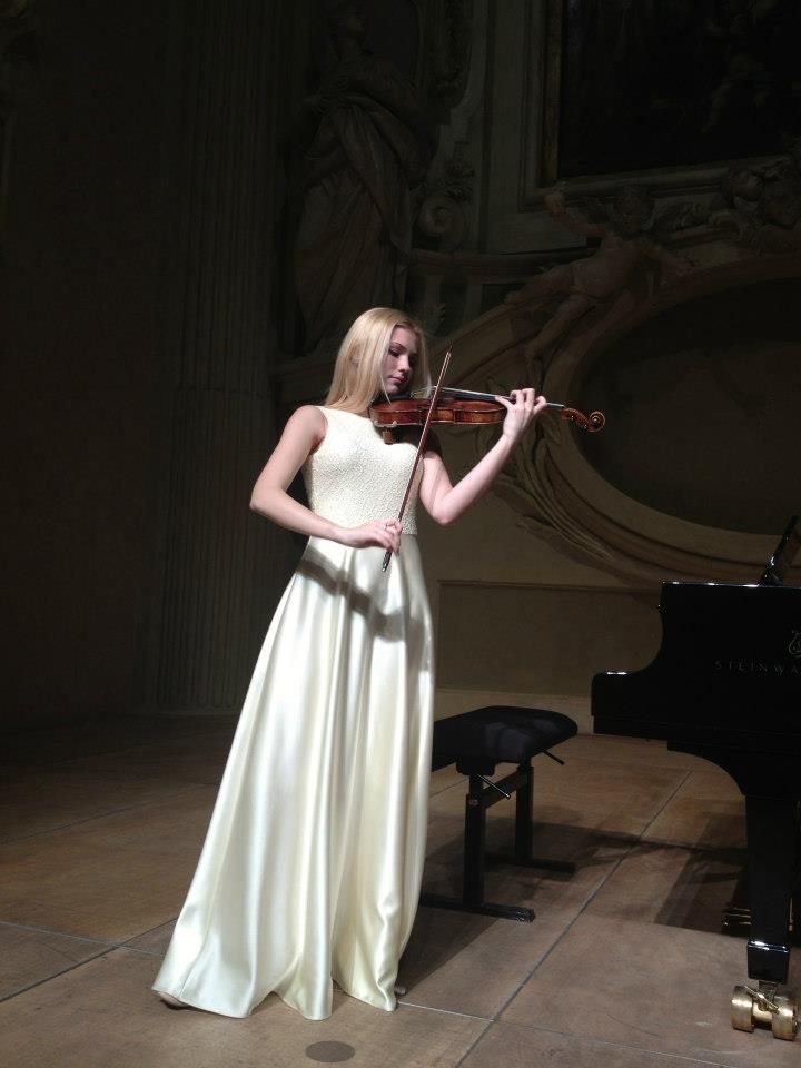 a woman in a white dress is playing the violin and standing next to a grand piano