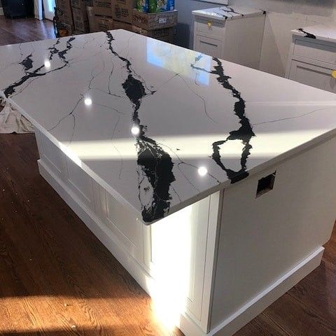 a kitchen island with marble counter tops in the middle of a hardwood flooring area