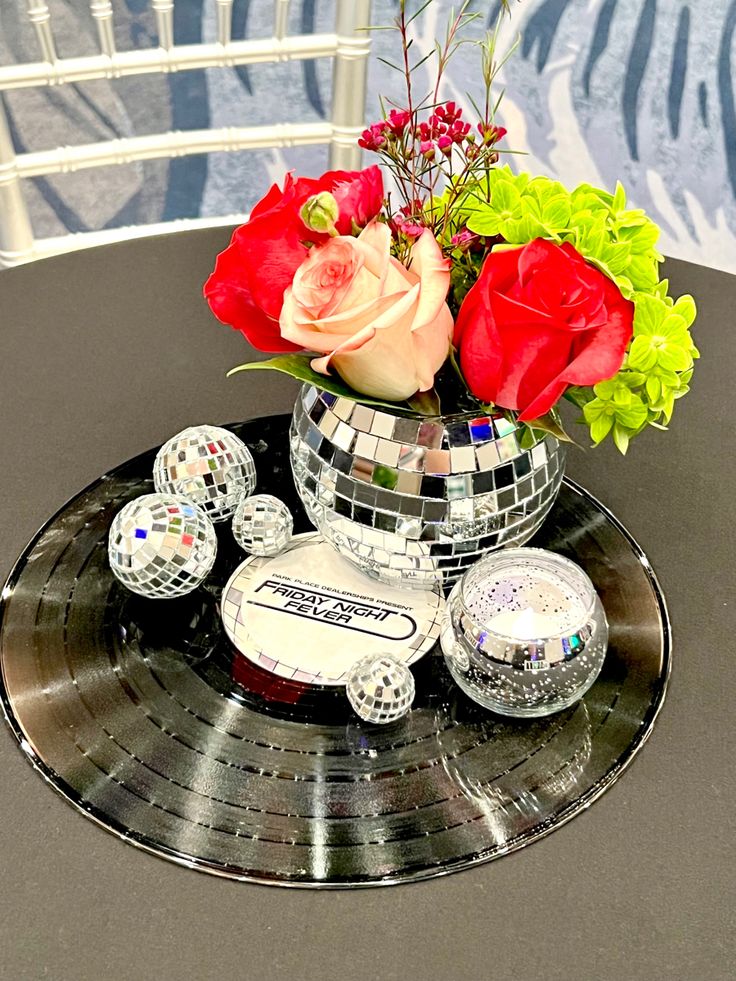 a disco ball centerpiece with roses and other decorations on a round metal table top