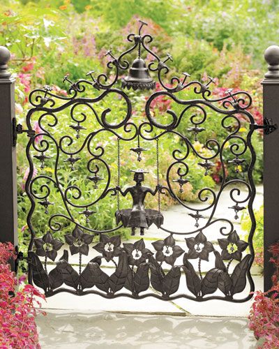 an iron gate with cats on it and flowers in the foreground, surrounded by greenery