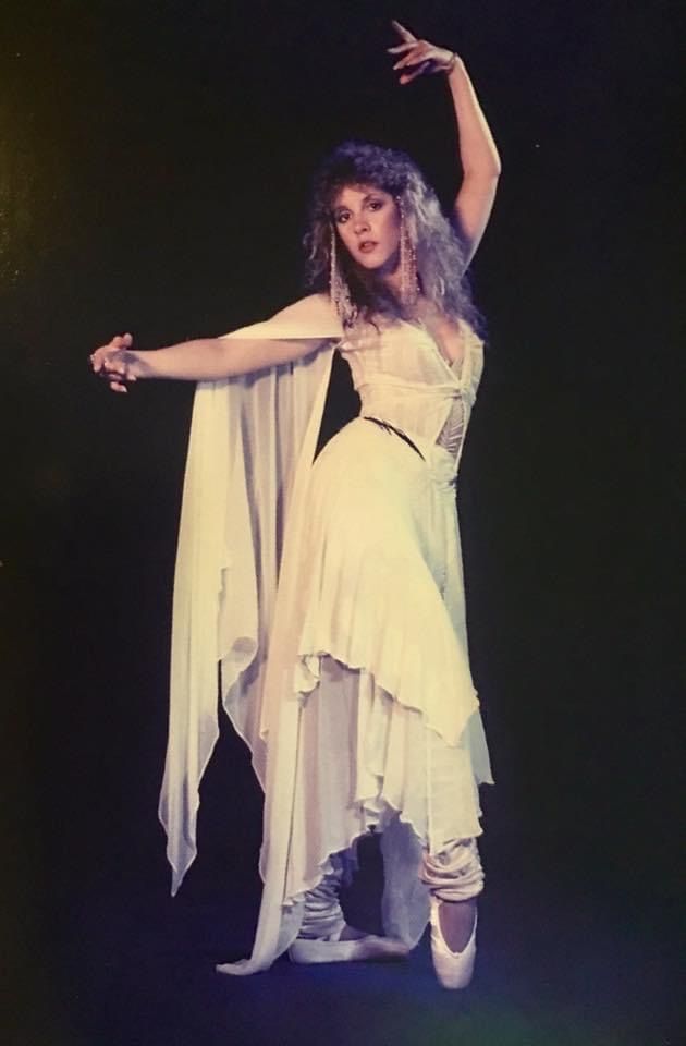 a woman dressed in white is dancing with her arms spread out and hands extended to the side