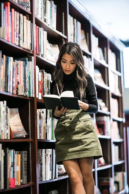 a woman standing in front of a bookshelf holding a book and looking at it