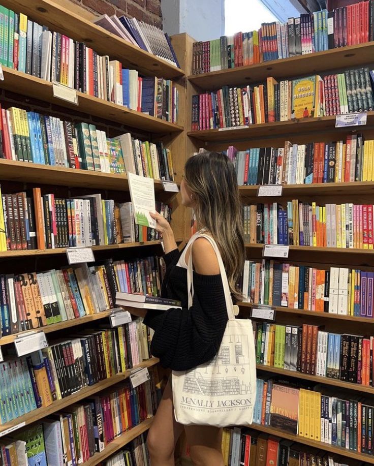 a woman reading a book in front of a bookshelf full of colorful books