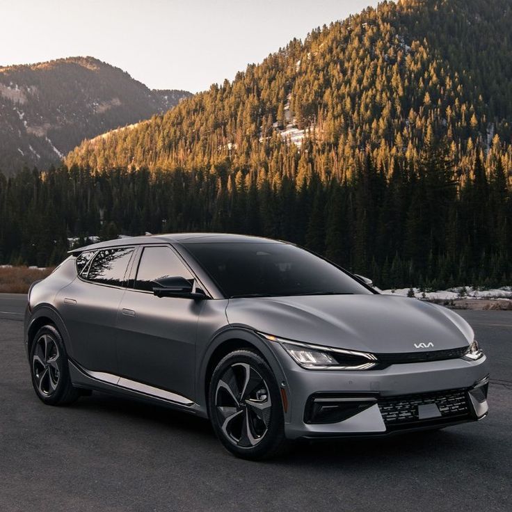 a gray sports car is driving down the road in front of mountains and pine trees