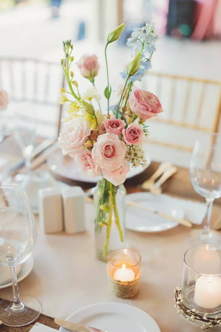 the table is set with white plates and silverware, pink flowers in a vase