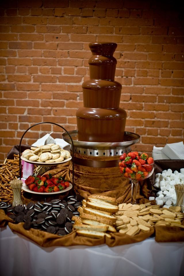 a table topped with lots of food and desserts next to a red brick wall