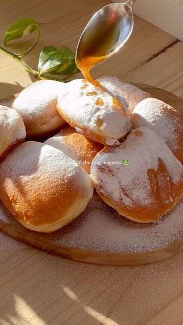 powdered donuts sit on a wooden plate with a spoon pouring syrup onto them