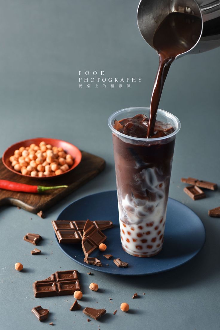 chocolate milkshake being poured into a cup with cocoa and peanuts on the side