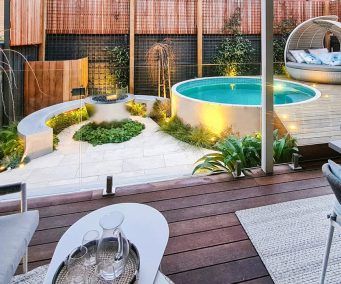 a backyard with a swimming pool surrounded by greenery and wooden fenced in area