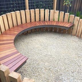 a wooden bench sitting in the middle of a gravel area next to a wood fence