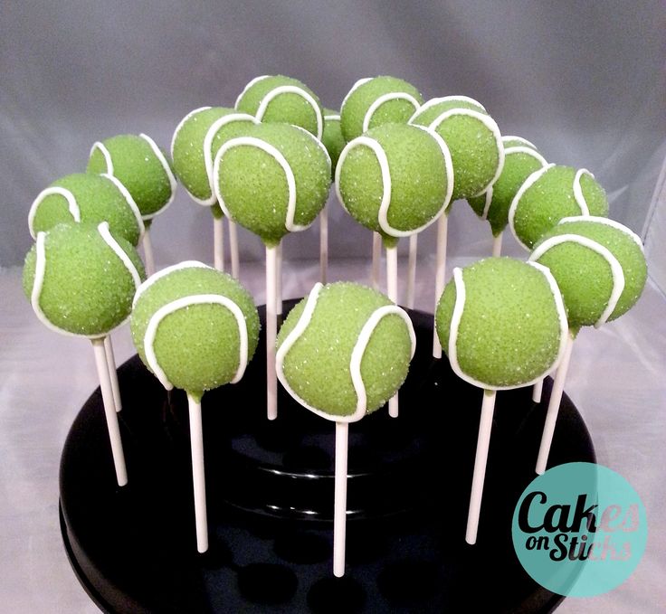 tennis ball cake pops on a black plate with white icing and green sprinkles