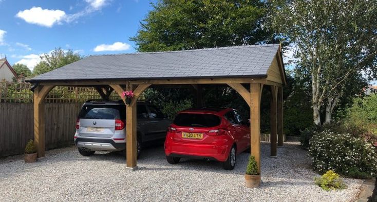 two cars are parked under a wooden carport