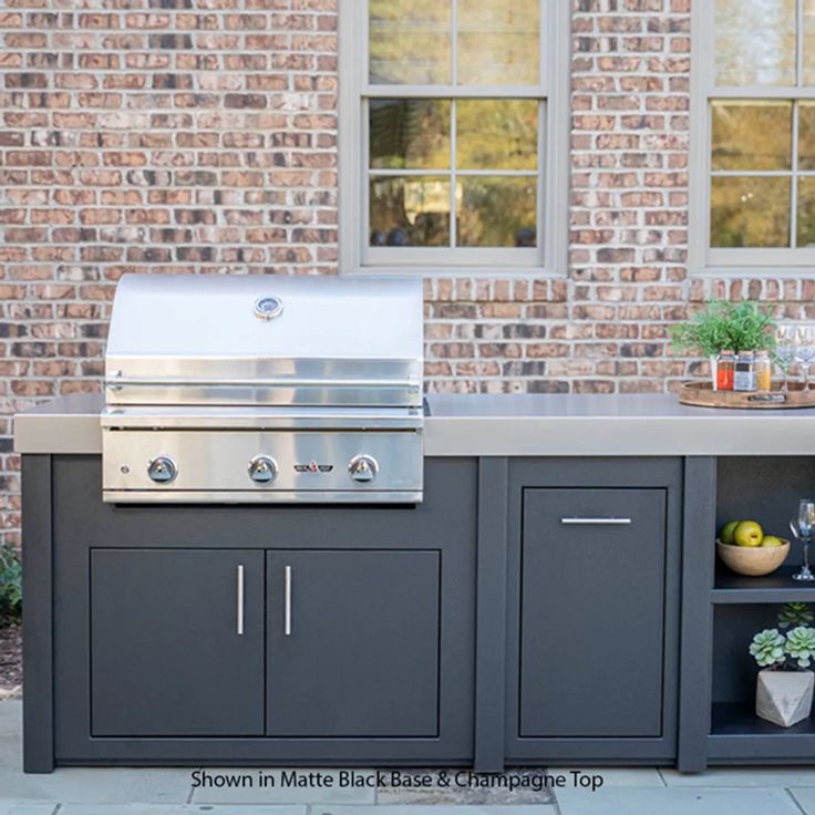 an outdoor kitchen with built - in grill, sink and countertop on the side of a brick building