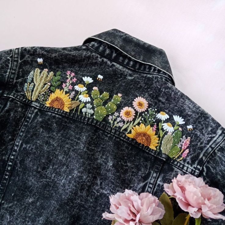 a denim jacket with embroidered flowers and cactus on the back, next to pink carnations