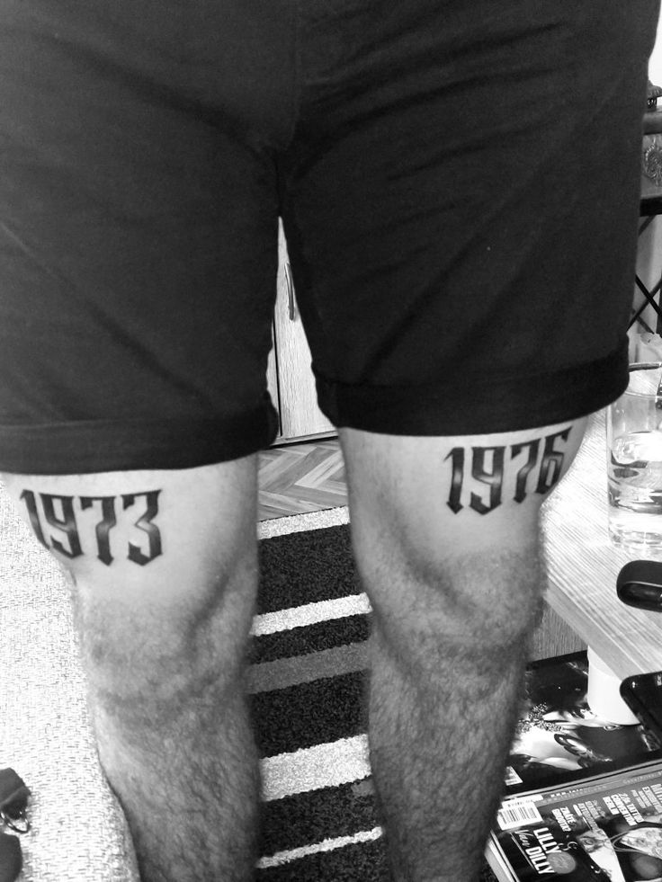 black and white photograph of legs with tattoos on them, standing in front of books